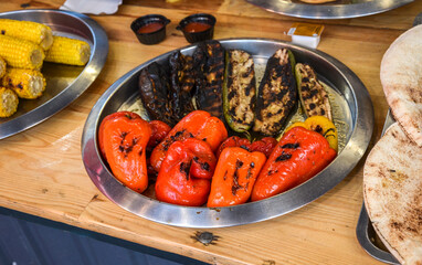 Silver platter on a wooden table holds a delicious assortment of grilled vegetables, including charred eggplant, zucchini, and vibrant red and orange bell peppers 
