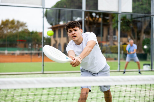 Portrait of young sporty guy playing paddle tennis with friends on open court. Active lifestyle concept