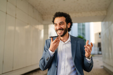 Smiling businessman using smart phone voice assistant outdoors