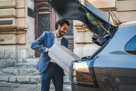 Businessman loading luggage into car trunk on city street