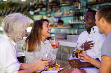 Cheerful international friends different ages enjoying pinchos and beer in the evening pub