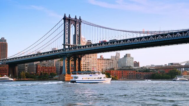 Riverboat moves by the waterscape under the Manhattan Bridge. Buses move by the highway on the bridge. New York, USA.