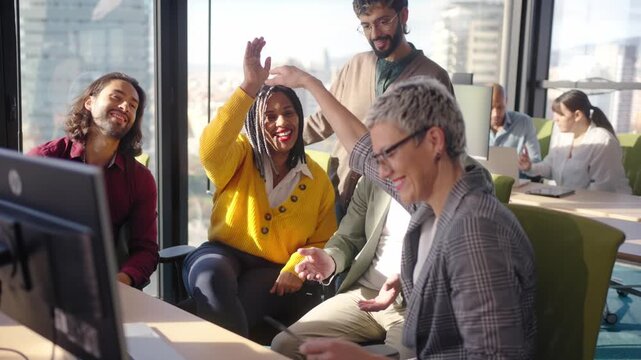 Multicultural team celebrating a milestone with a high five in a bright modern office, showing positive energy, collaboration and motivation while colleagues smile and keep working.