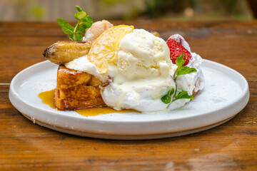 Delectable French toast dessert with ice cream, strawberries, and syrup on a white plate
