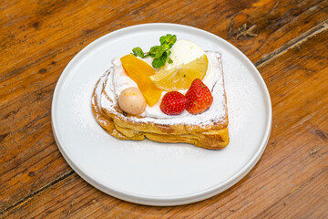 Delicious gourmet dessert toast with fresh fruit, cream, and mint on a wooden table setting