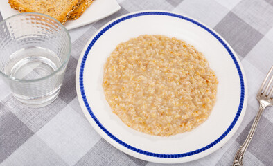Boiled oatmeal porridge served in white plate. Concept of diet food