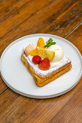 Delicious gourmet toast with fresh fruit, ice cream, and mint on a rustic wooden table
