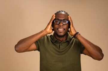 Smiling African man in green polo shirt and eyeglasses holding head with both hands in studio. Concept of surprise, realization, joy, and lifestyle expression.