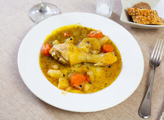 plate of fried chicken leg and vegetable stew of potatoes and carrots sits on table covered with checkered tablecloth.selective focus