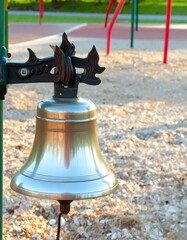 Polished metal bell hangs on a post in a playground