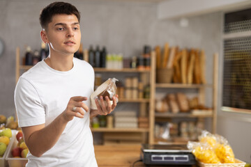 Attentive young guy is choosing different types of cheese in grocery store