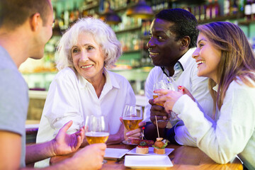 Spending time in bar. Four positive friends drinking beer in bar