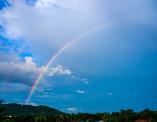Colorful rainbow arches over a partly cloudy sky and hills