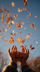 Autumn leaves falling from cupped hands against a clear blue sky