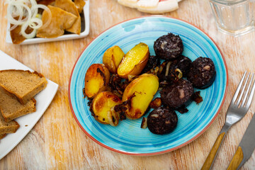on table served for dinner is plate of fried blood sausages and potatoes in their skins, garnished with bacon, bran bread and pita