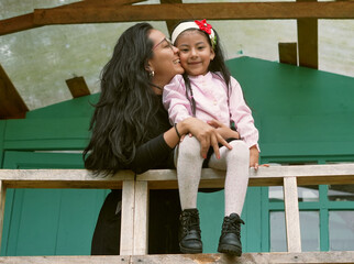 Latin american mother kissing daughter on wooden porch railing