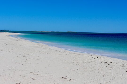 Empty sandy beach with turquoise ocean and clear blue sky.