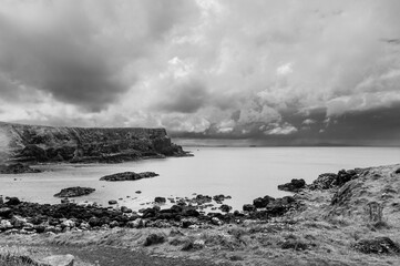 A black and white photo of a rocky shoreline with a stormy sky in the background