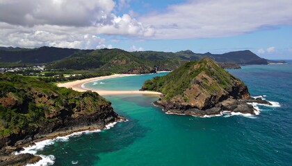 Fototapeta premium A high-angle, expansive view of a secluded bay, showcasing turquoise waters, a sandy beach, and lush greenery-covered hills.