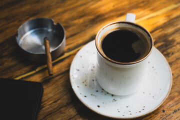 Coffee, smartphone and cigar on wooden table. Lifestyle concept with coffee, phone and cigar. Morning coffee with technology and luxury cigar. Cigar, coffee and smartphone on wooden surface.