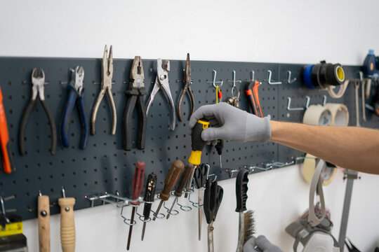In a workshop setting, a person in gloves carefully selects a tool from a neatly organized pegboard, highlighting focus and preparation for a task ahead.