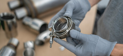 Mechanic holds a v-band exhaust component with focus on details, while preparing for assembly in an automotive repair workshop setting.