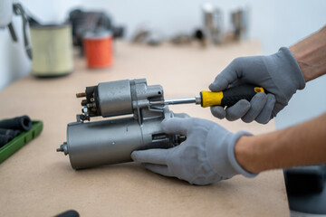 A person works on fixing a car starter using a screwdriver and wearing gloves in a well-lit...