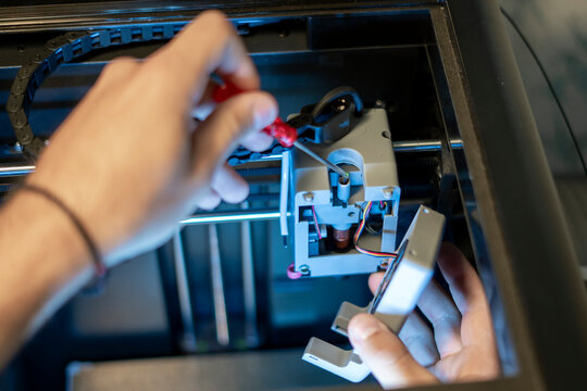 A person is closely working on the internal mechanism of a 3D printer using a screwdriver, ensuring proper functionality in a workshop setting.