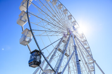 Obraz premium Giant ferris wheel against bright blue sky with sunburst