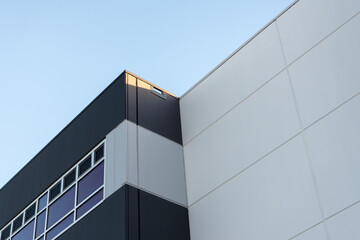 The top floors of a large contemporary building with metal composite panels on the exterior. The modern commercial building has light grey and black panels with multiple square shaped glass windows.