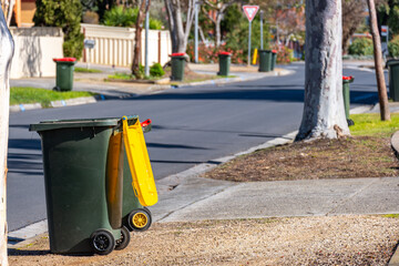 Household wheelie bin with a yellow recycling lid placed on the curb of a suburban street in...