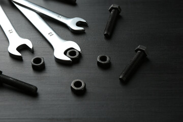 Many metal wrenches, bolts and nuts on black wooden table, closeup