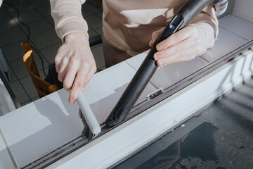 Hands of a man vacuums debris from the window frame.