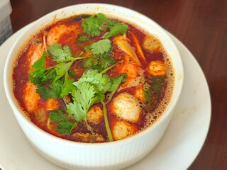Hot and steamy bowl of tom yum soup with shrimp, mushrooms, and herbs in a spicy red broth, served fresh in a white ceramic bowl.