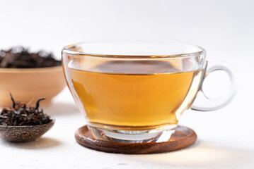 Black tea in cup glass with dried tea leaves on white background, Healthy herbal hot drink