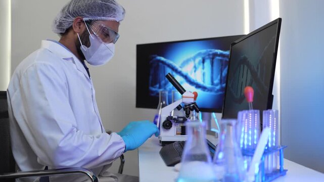 A geneticist performs microscopic analysis of a cellular sample, cross-referencing observations with genomic data displayed on a bioinformatics workstation in a biotech lab.