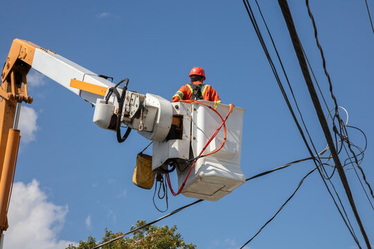Electrical lineman in bucket truck working on power lines against blue sky