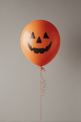 An orange balloon with a simple black flat icon of a Halloween jack o lantern printed on it, isolated on a white background