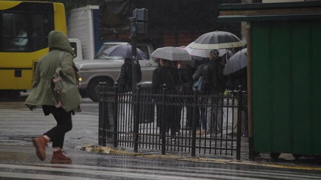 Torrential rain in Buenos Aires, Argentina. Daytime city scene with heavy rainfall, people under umbrellas, cars on wet streets, water puddles splashing, trees, buildings, and urban life. 4K 10-bit fo