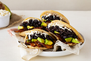 Venezuelan arepas with black beans, avocado, fried plantains, and cheese on rustic background