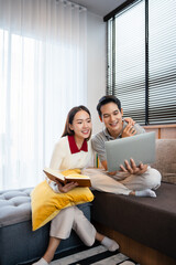 Fototapeta premium happy young couple relaxing together on the sofa at home and reading book and using laptop computer . couple having a conversation together while relaxing on the couch. Copy space.