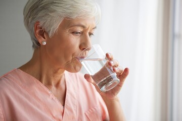 Senior Woman Drinking Water by Window - Healthy Lifestyle and Hydration Concept