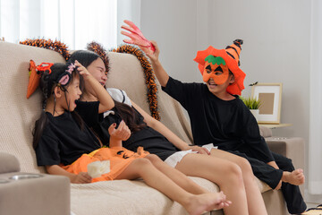 Girls wear spooky costumes, one wears an orange headpiece and mask, another a tutu, as a hand prank...