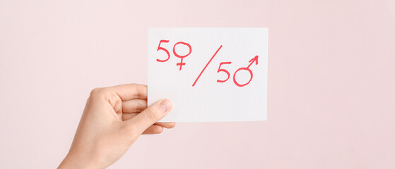 Female hand holding paper sheet with simple fraction and symbols of woman and man on color...