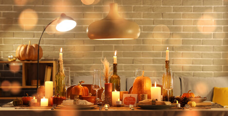 Festive table setting with burning candles, pumpkins and greeting cards for Thanksgiving Day at evening