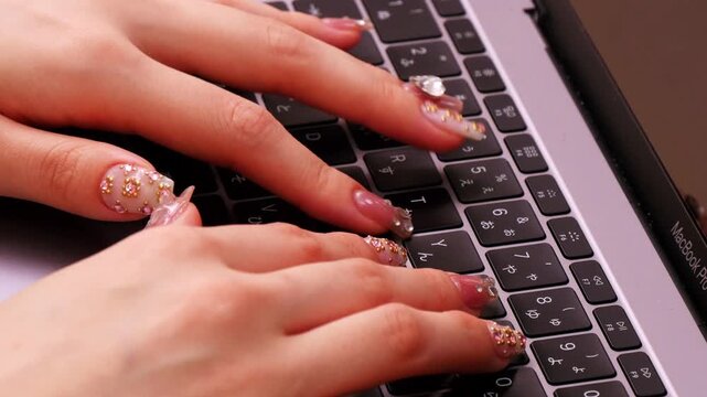 ノートパソコンのキーボードを操作するネイルアート女子の手元