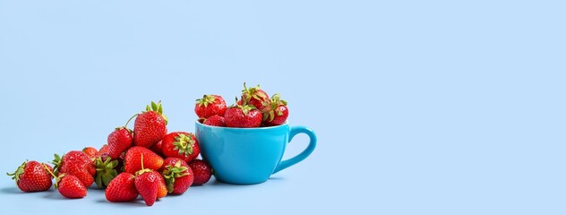 Cup and fresh ripe strawberries on blue background with space for text