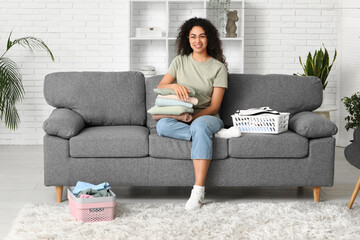 Beautiful young happy African-American woman folding clean clothes at home