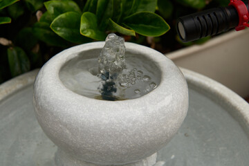 Microphone recording the tranquil sound of a small stone water fountain in a lush green garden.