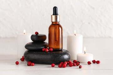 Composition with bottle of natural essential oil, spa stones, burning candles and hawthorn on light wooden table
